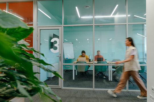 Businesswoman walking near businessmen working on laptop in office