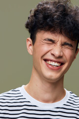 Fototapeta premium smiling man with curly hair in striped shirt laughing with closed eyes, natural joyful expression, studio portrait with muted green background