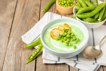 Green pea soup on a wooden table. Fresh pea soup bowl. Delicious healthy cream soup in a bowl with green peas and croutons. Healthy vegan puree. Copy space. Space for text.