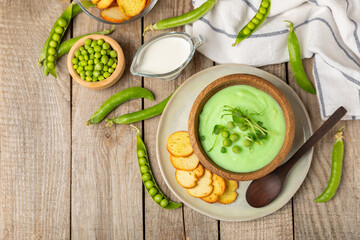 Green pea soup on a wooden table. Fresh pea soup bowl. Delicious healthy cream soup in a bowl with green peas and croutons. Healthy vegan puree. Copy space. Space for text.
