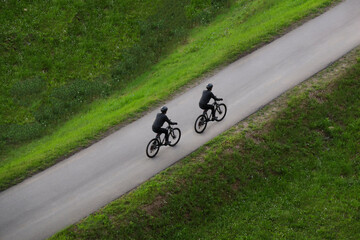 Aerial top view of 2 two Cyclist with helmet riding on sporty cross bicycle on asphalt road grass background Mens ride bike on an empty road with white lines. male wearing black helmet clothes