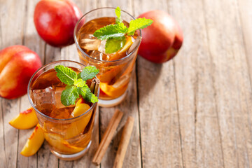 Refreshing peach iced tea in glass with ice cubes and cinnamon on wooden table. Copy space