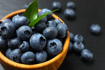 Blueberries in a wooden bowl on black background. Dark blue colored, ripe, raw berries. Food photo.