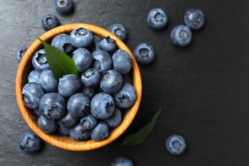 Ripe blueberries in a wooden bowl on a background of scattered berries. Healthy and dietary nutrition concept. Top view.