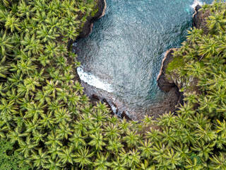 Tropical Rolas Island on São Tomé aerial view with black volcanic rocks, white sand, turquoise water and lush green palm forest.