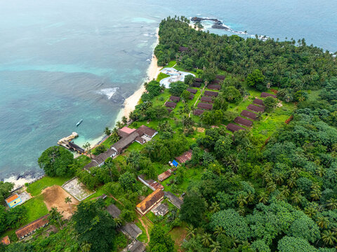 Aerial view of a small village on Rolas Island, S&atilde;o Tom&eacute; and Pr&iacute;ncipe, surrounded by dense tropical jungle and simple tin-roof houses.
