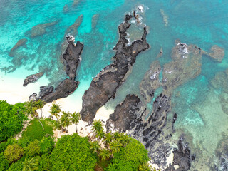 Tropical  Rolas Island on São Tomé aerial view with black volcanic rocks, white sand, turquoise water and lush green palm forest.