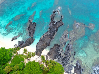 Tropical  Rolas Island on São Tomé aerial view with black volcanic rocks, white sand, turquoise water and lush green palm forest.