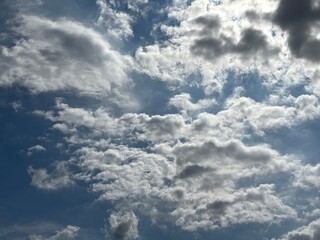 Obraz premium Bright blue sky with a smooth spread of white clouds, sunlight is seen spreading softly from behind the cloud layer in the middle, creating a calm and peaceful atmosphere.