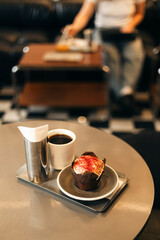 Cup of black coffee and muffin with white icing and red sprinkles on a table.