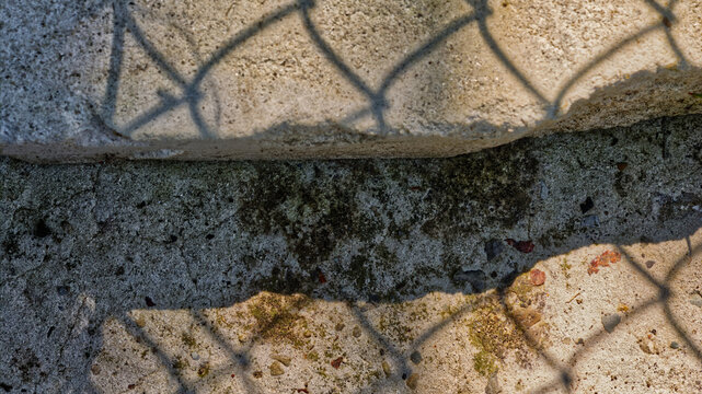 Abstract background of a chain-link fence shadow on a two-level concrete surface. Grunge urban texture representing division, borders, and separation. High contrast with ample copy space.