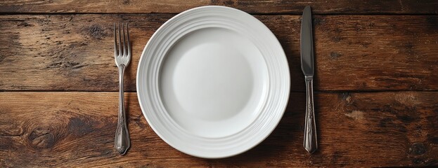 Empty white plate and cutlery on a rustic wooden table