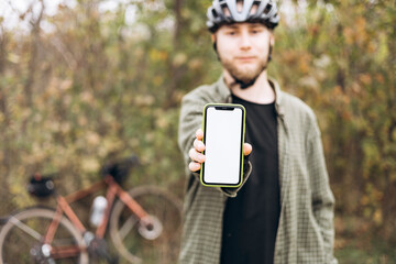 Cyclist in helmet holding smartphone with blank white screen and showing it.