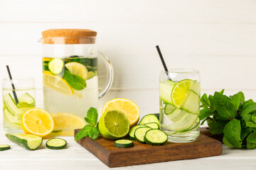 Cucumber water with lemon, lime and mint on a wooden table. Water infused with sliced ​​cucumber in a drinking glass. Tonic refreshing drink. Cucumber lemonade.Summer natural cooling drink.Copy space