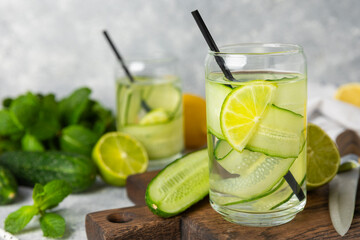 Cucumber water with lemon, lime and mint on a wooden table. Water infused with sliced ​​cucumber in a drinking glass. Tonic refreshing drink. Cucumber lemonade.Summer natural cooling drink.Copy space