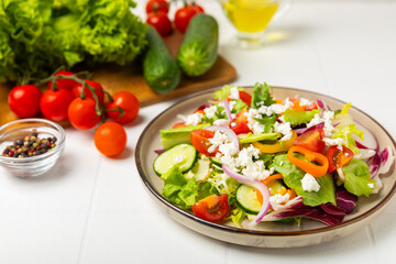 Cucumber salad on a wooden background.Homemade salad with fresh vegetables, cucumber, tomato, sweet pepper and lettuce in a plate.Vegetarian spring salad.Vegetarian diet.Healthy eating.Space for text
