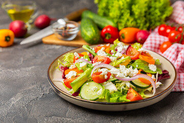 Cucumber salad on a wooden background.Homemade salad with fresh vegetables, cucumber, tomato, sweet pepper and lettuce in a plate.Vegetarian spring salad.Vegetarian diet.Healthy eating.Space for text