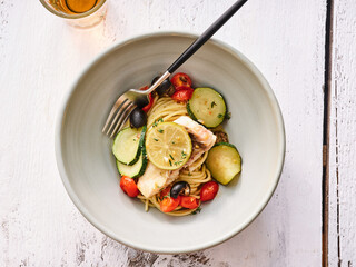 This appetizing bowl showcases a hearty serving of spaghetti topped with tender pieces of cod, fresh zucchini slices, and vibrant cherry tomatoes. Perfect for a lunch