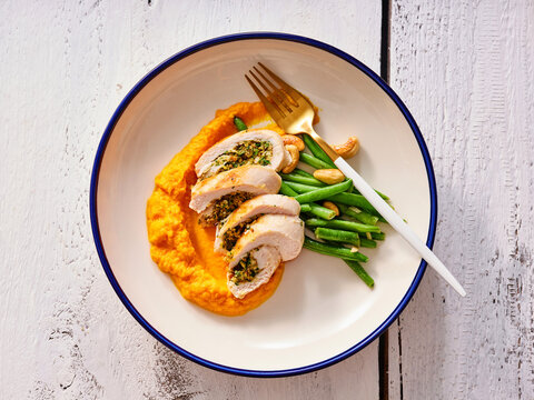 A tantalizing dish features garlic and herb stuffed chicken alongside creamy sweet potato mash and fresh green beans. Ideal for a nutritious and flavorful dinner option
