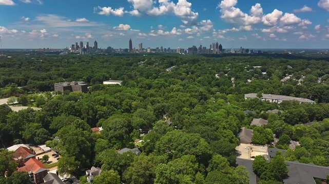 Junction in luxury suburb district of Atlanta. Single family houses and one family homes in American town. Green trees in summer. Downtown skyline with skyscrapers in background. Aerial tilt down shot