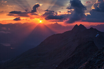 Fototapeta premium Sunset view from Piz Languard towards the western Alps – violet sky and glowing sun rays over rugged peaks in the Swiss Alps