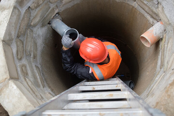 Worker in protective gear installing and inspecting septic system pipes inside a manhole at a...