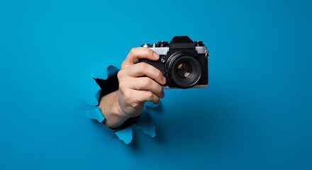 Hand with Vintage SLR Camera Bursting Through Torn Blue Paper Wall