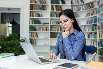 A young woman sits at a desk in a library surrounded by books, working intently on her laptop. The serene environment emphasizes learning, concentration, and productivity.