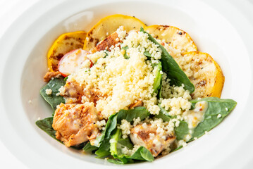 Grilled chicken with creamy sauce, couscous, spinach, and yellow squash slices served on a plate. Healthy, colorful, and balanced meal presentation