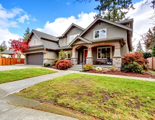 Classic American two-story house with a garage and well-maintained green lawn, surrounded by colorful landscaping on a sunny day.