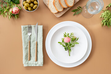 Festive table setting with empty plate, cutlery and napkin - flowers decorated, bread and olives...