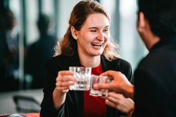 Smiling businesswoman clinks glasses with a colleague during a relaxed after-work celebration. A cheerful moment of connection, casual networking, and professional camaraderie over drinks.