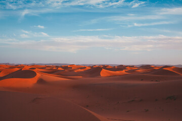 Endless sand dunes of the Lion Dune, Morocco – vast desert landscape at red sunset, dramatic sky over rolling dunes, serene and majestic Sahara desert scenery