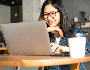 Happy Young Asian Businesswoman Working on Laptop in Coffee Shop – Online Meeting, Remote Work, and Digital Nomad Lifestyle