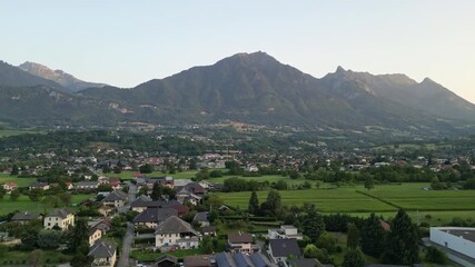 Aerial drone panorama of a French alpine city in the Savoie Alps during a bright summer morning, with warm sunlight illuminating Albertville and the surrounding mountains and valley landscape.