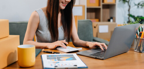 Business owner using calculator and smart phone working at home office.