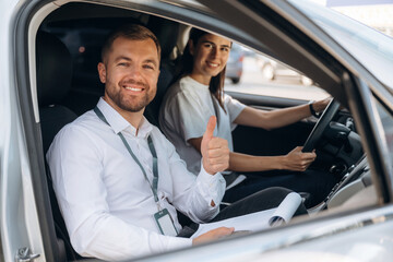 Gesture of thumb up, smiling. Woman is with instructor in car, driving school concept