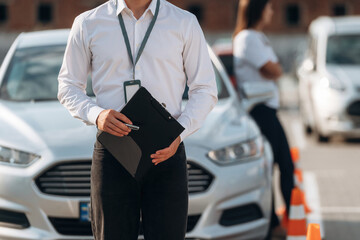 Documents in hands of a guy. Man instructor in the driving school and woman are outside the car