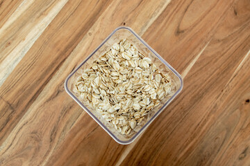 Uncooked oat flakes in transparent plastic container on the table.