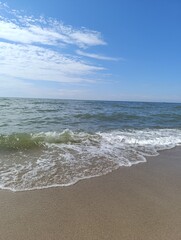 Seascape with gentle waves lapping on sandy shore under blue sky  