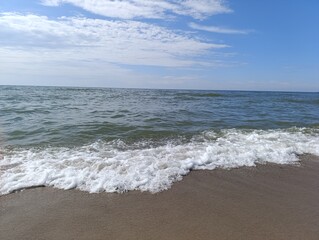 Coastal waves gently rolling onto sandy beach under blue sky  