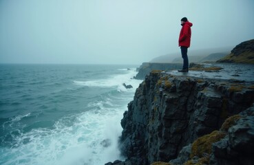 Man standing on rocky cliff overlooking the ocean on a cloudy day