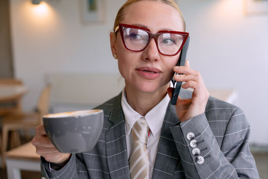 Businesswoman talking on the phone while enjoying coffee in a modern cafe during the day