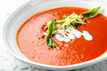 Bowl of tomato soup with basil, shredded cucumber, and cream drizzle. Vibrant red color with fresh green and white garnish. Restaurant-style food presentation