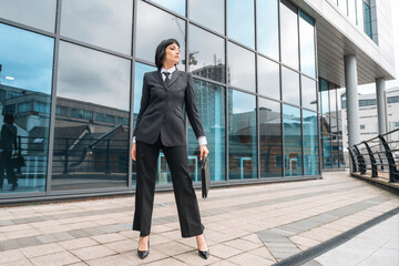 Confident woman in tailored suit stands outside modern building during daytime showcasing...