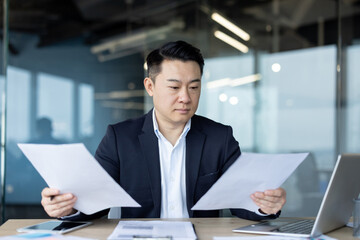 Asian young man in a suit sitting in the office at his workplace and working with documents and a project