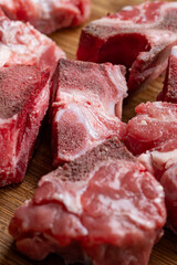 Raw, cut, fresh beef ox tail pieces used for soup broth or stews. Top down view, set on wooden kitchen board, close up shot, no people