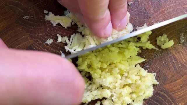 Minced garlic being squeezed out of a garlic press directly onto a wooden cutting board