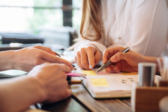 Planning the project, working. Close up view of young people sitting by the table indoors - Powered by Adobe