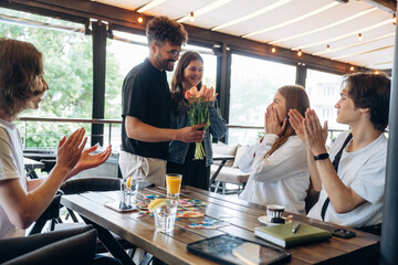 Celebrating the birthday, giving flowers. Group of young friends are in the cafe restaurant
